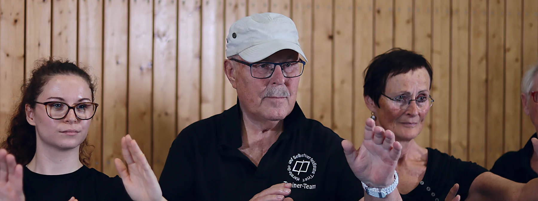 Arnold Panschar, Gründer des Vereins, mit Kappe und Vereinsshirt im Training, neben ihm zwei Teilnehmerinnen